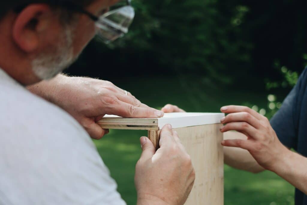Two people attaching two wood boards together at a 90 degree angle.

Photo by Jessica Mangano